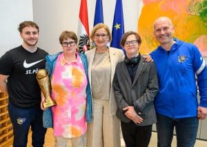 5 Personen, davon 1 Spieler und 2 Spielerinnen des Special Needs Teams, Landeshauptfrau Mikl-Leitner und der Trainer mit grauem Haar und Blauer Trainingsjacke stehen lachend vor drei Flaggen für Österreich, Niederösterreich und EU.