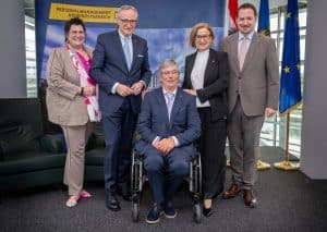 Zwei Frauen und drei Männer posieren vor einer Land-Niederösterreich Leinwand. Der Herr in der Mitte sitzt im Rollstuhl, die anderen stehen.
